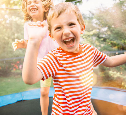 girl and boy jumping on trampoline lauging