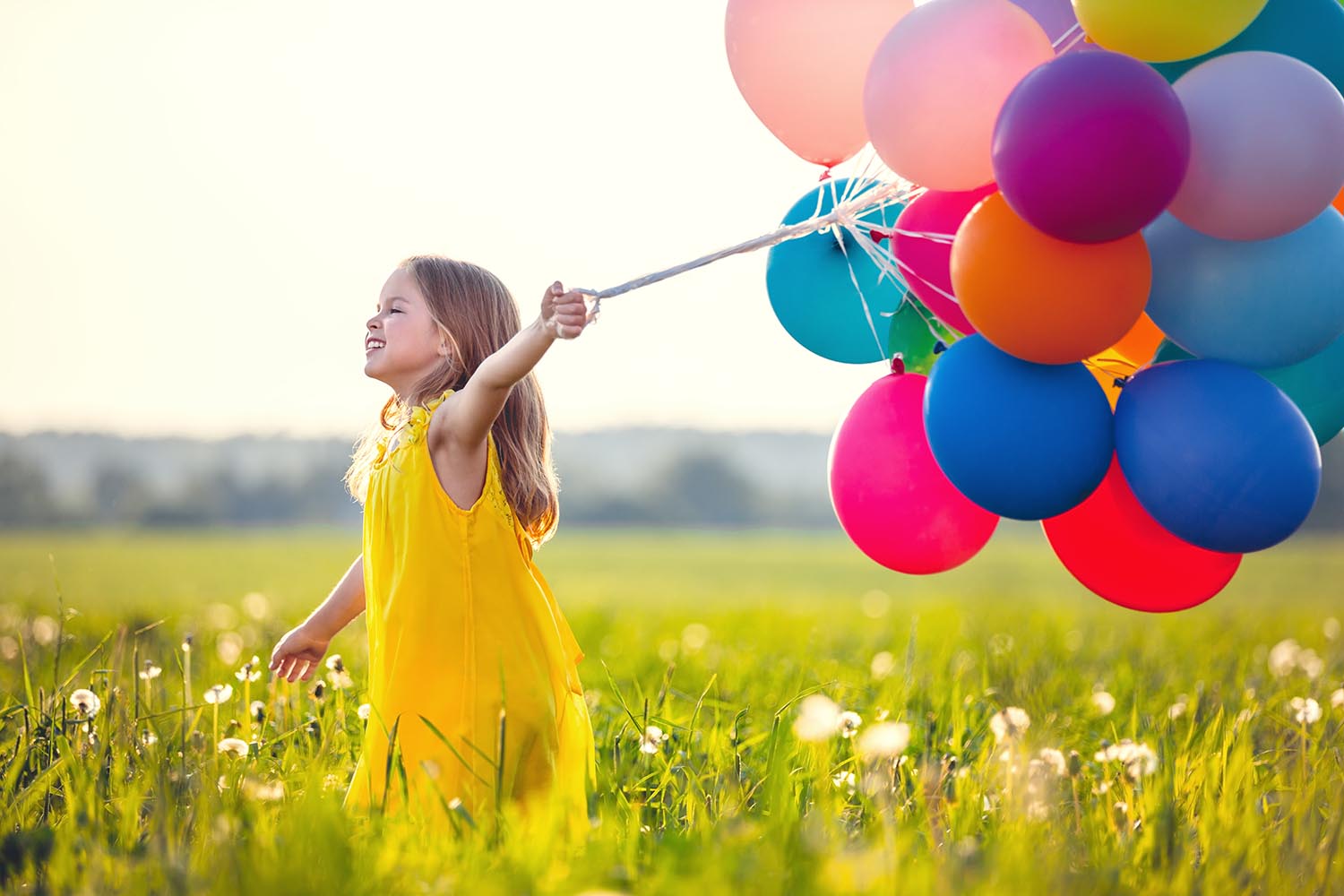Girl holding baloons walking in a field.