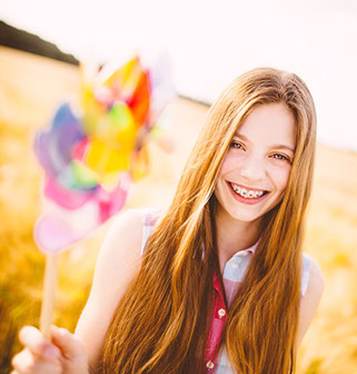 Girl with braces on with pinwheel standing in a field